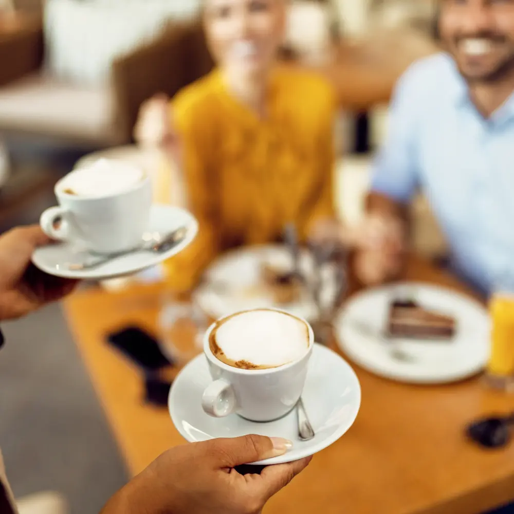 A barista serves two cups of coffee to smiling customers at a table