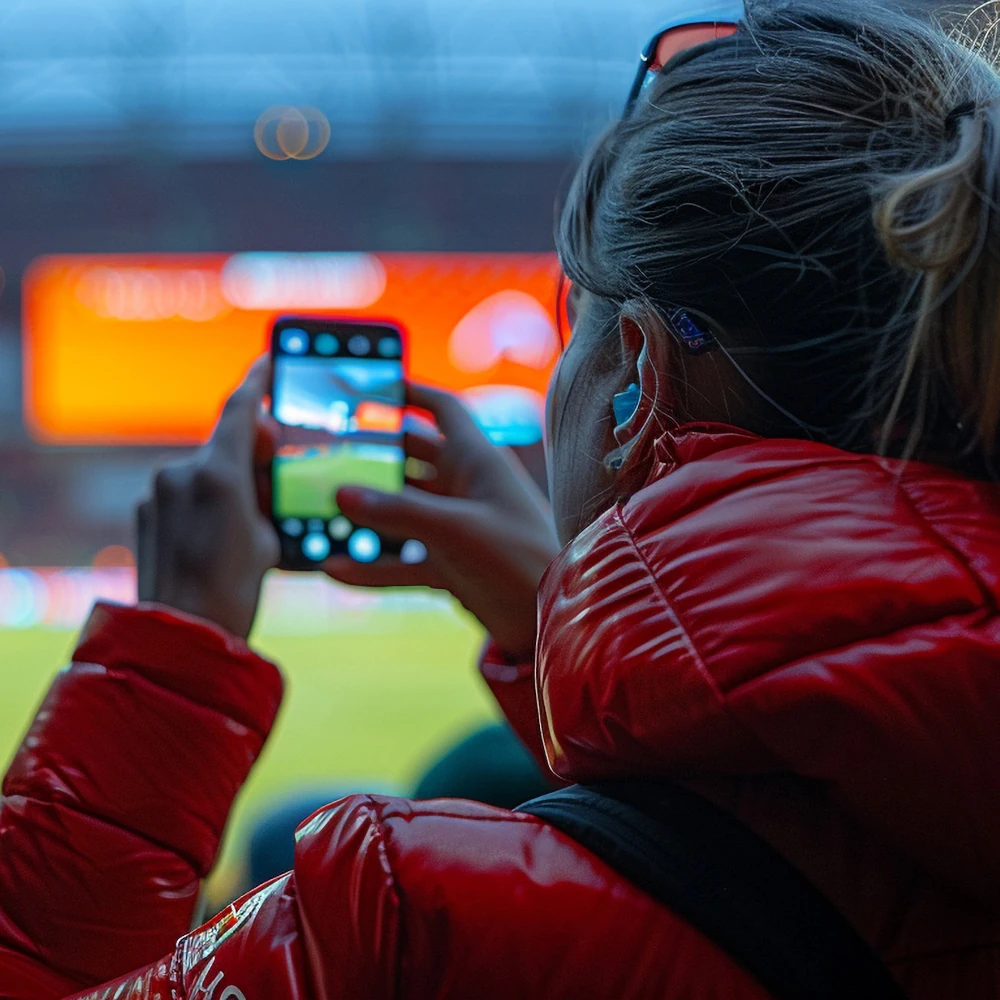 A woman taking a photo of a sporting event with her mobile phone